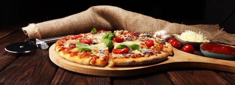Vegetarian Italian pizza with melted cheese, red tomatoes and green basil on a table decorated by cheese, tomato and red cherry tomatoes